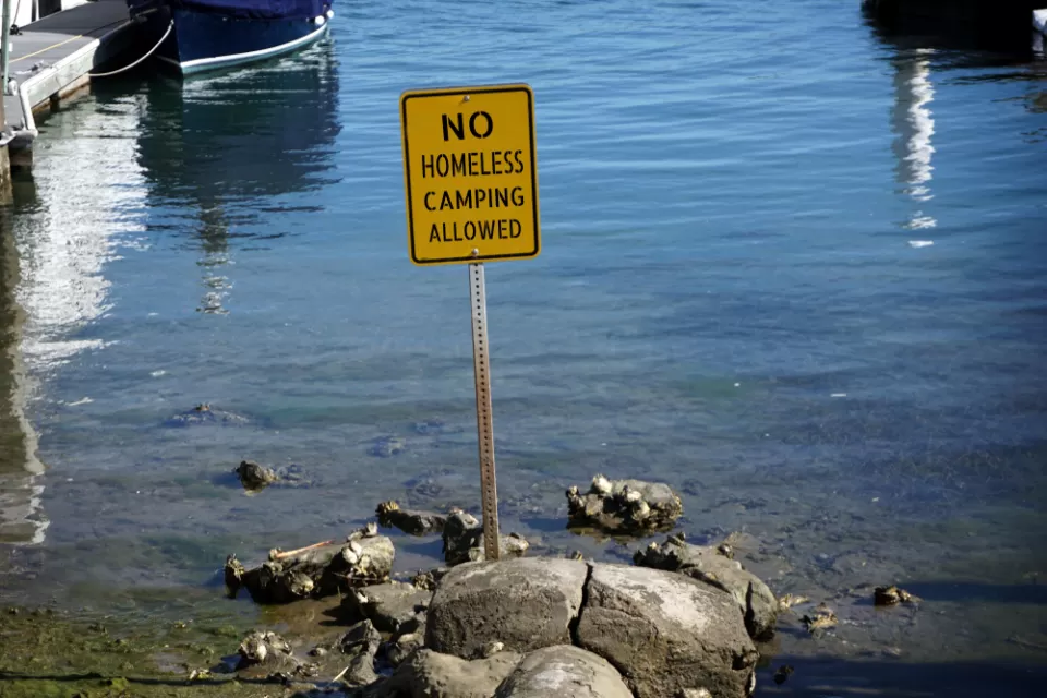 Yellow "no homeless camping" sign in water at California beach